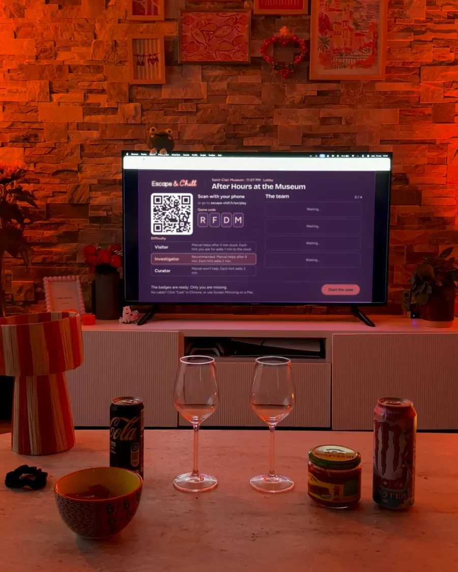 A dimly lit living room, the TV on in front of a coffee table with glasses